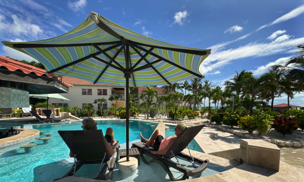 Guests relaxing under an umbrella by the pool at Belizean Shores Resort